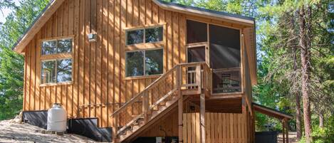 Een houten chalet met een trap naar een terras, omgeven door bomen.