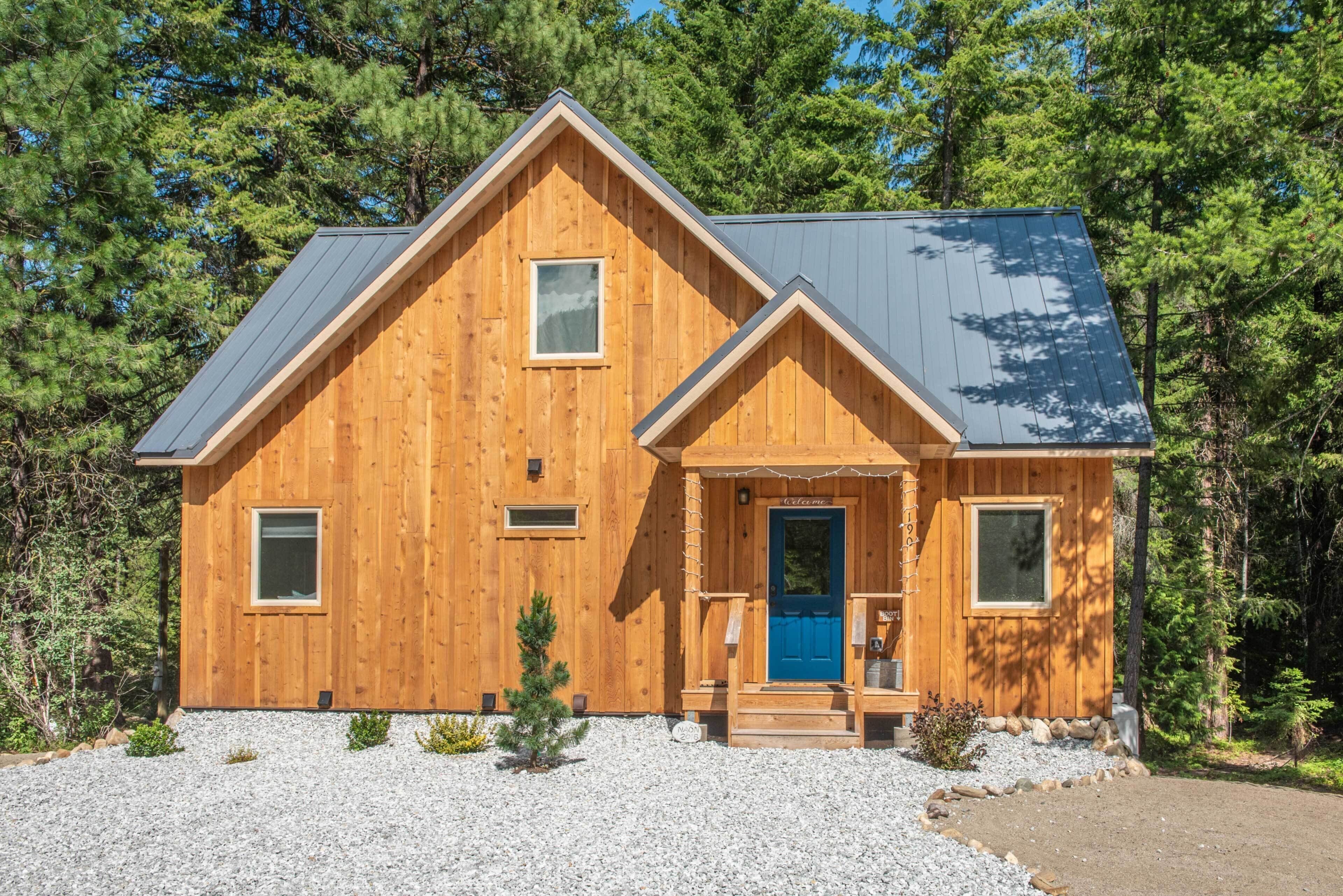 A wooden cabin with a blue door, a small porch, and a gravel driveway.