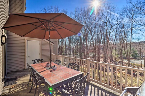 A covered outdoor patio with a table and chairs, a large umbrella, and a view of trees and hills.