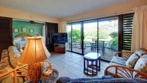 Ein Wohnzimmer mit einer Couch, einem Fernseher, einer Lampe und einer Schiebetür zu einer Außenpatio.