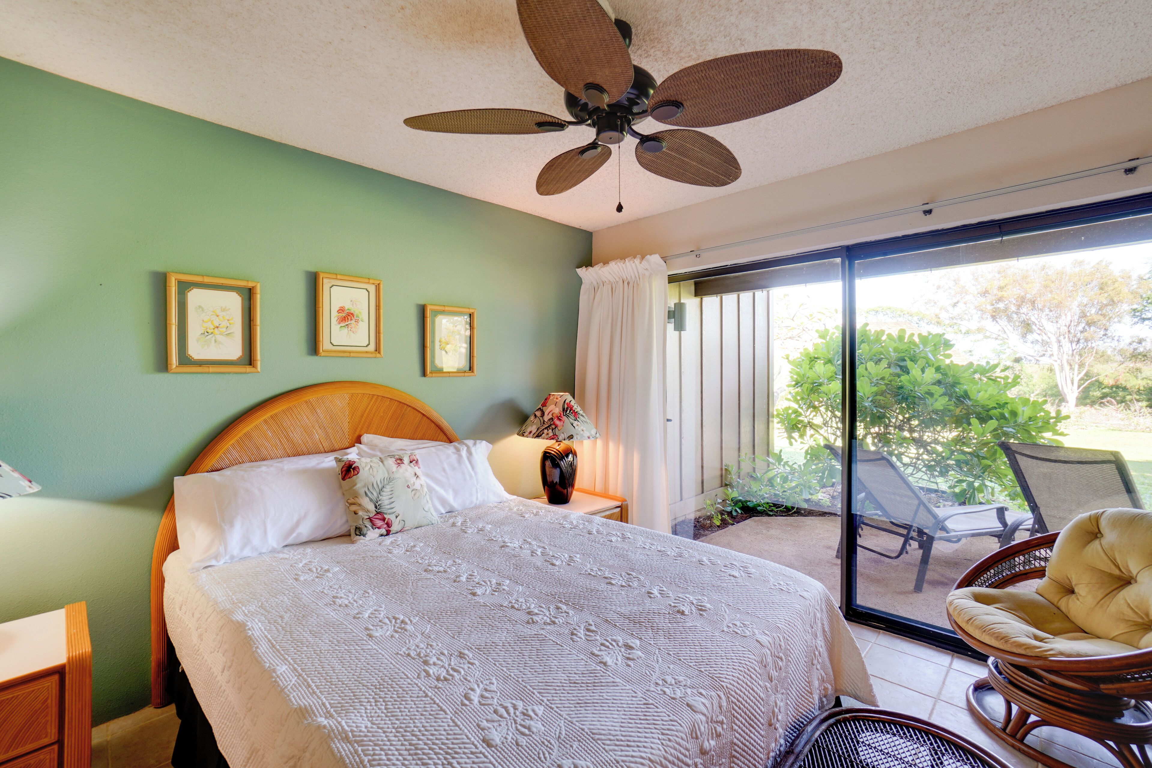 Quarto com cama grande, ventilador de teto, janela com cortinas e vista para o exterior.