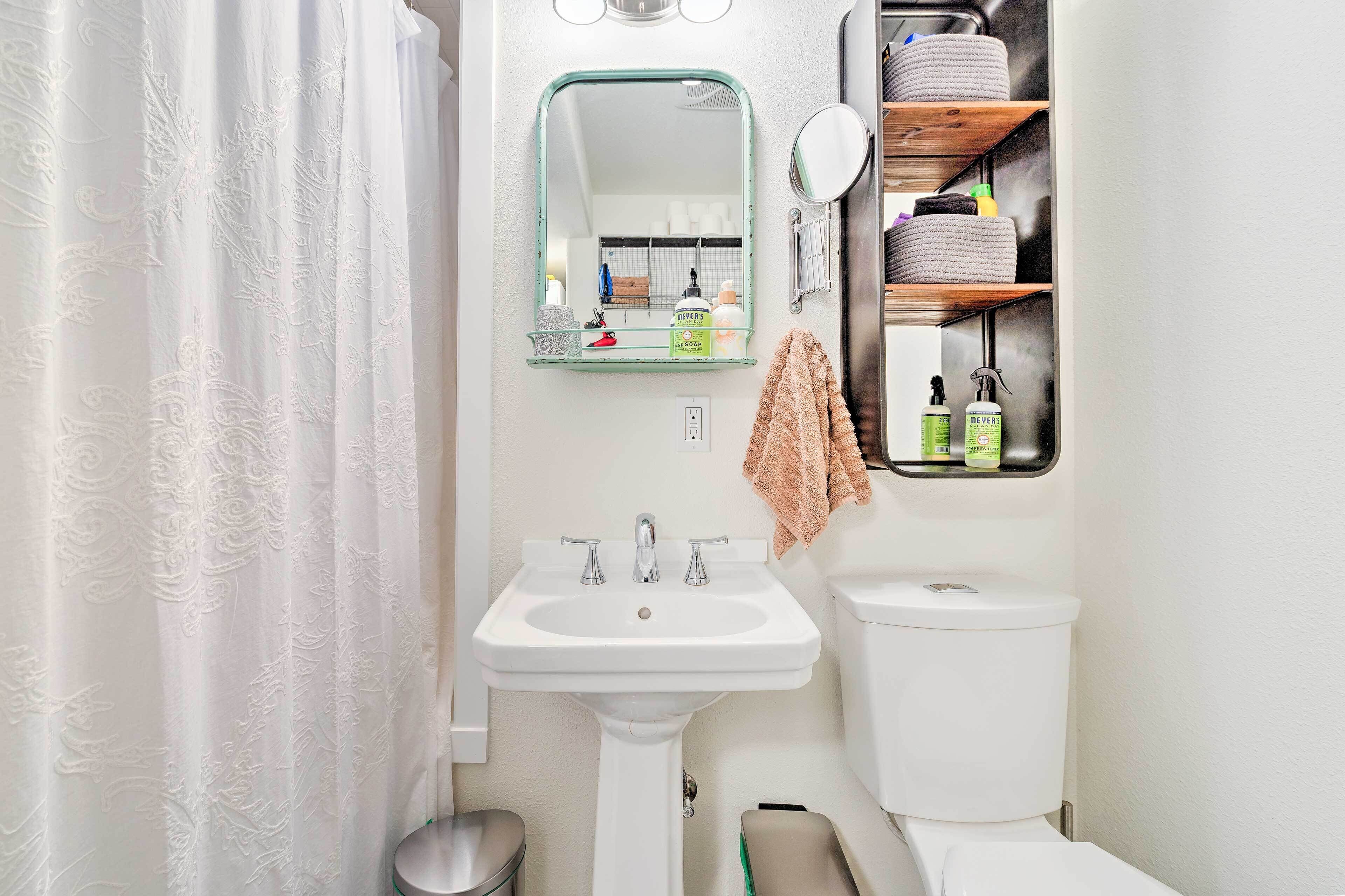 A bathroom with a white sink, two faucets, a toilet, a mirror, and a shelf with toiletries.