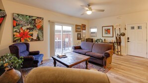 A living room with a sofa, armchair, coffee table, and a large painting. There is a door and a ceiling fan. - Bright Bend Home w/ Patio < 3 Mi to Downtown! (Bend)