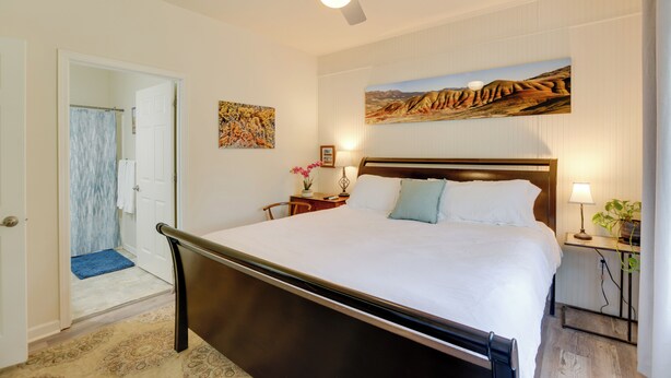 A bedroom with a bed, a ceiling fan, a nightstand with a lamp, a painting on the wall, and a bathroom visible through an open door. - Bright Bend Home w/ Patio < 3 Mi to Downtown! (Bend)