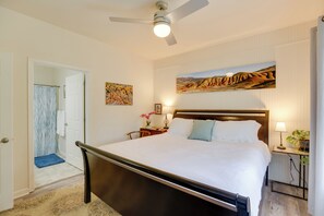 A bedroom with a bed, a ceiling fan, a nightstand with a lamp, a painting on the wall, and a bathroom visible through an open door. - Bright Bend Home w/ Patio < 3 Mi to Downtown! (Bend)