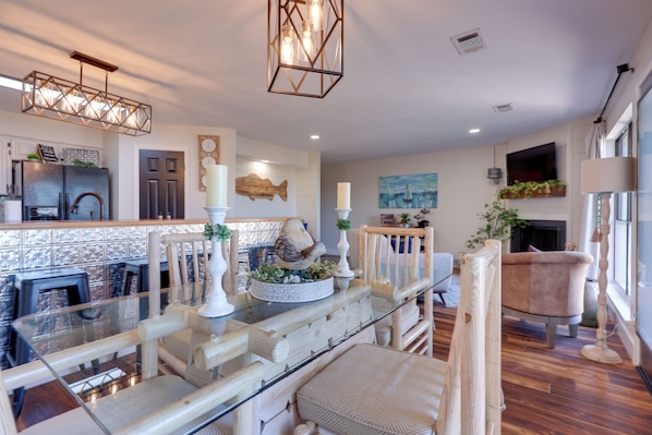 A modern kitchen with a glass dining table, wooden chairs, and a hanging light fixture.