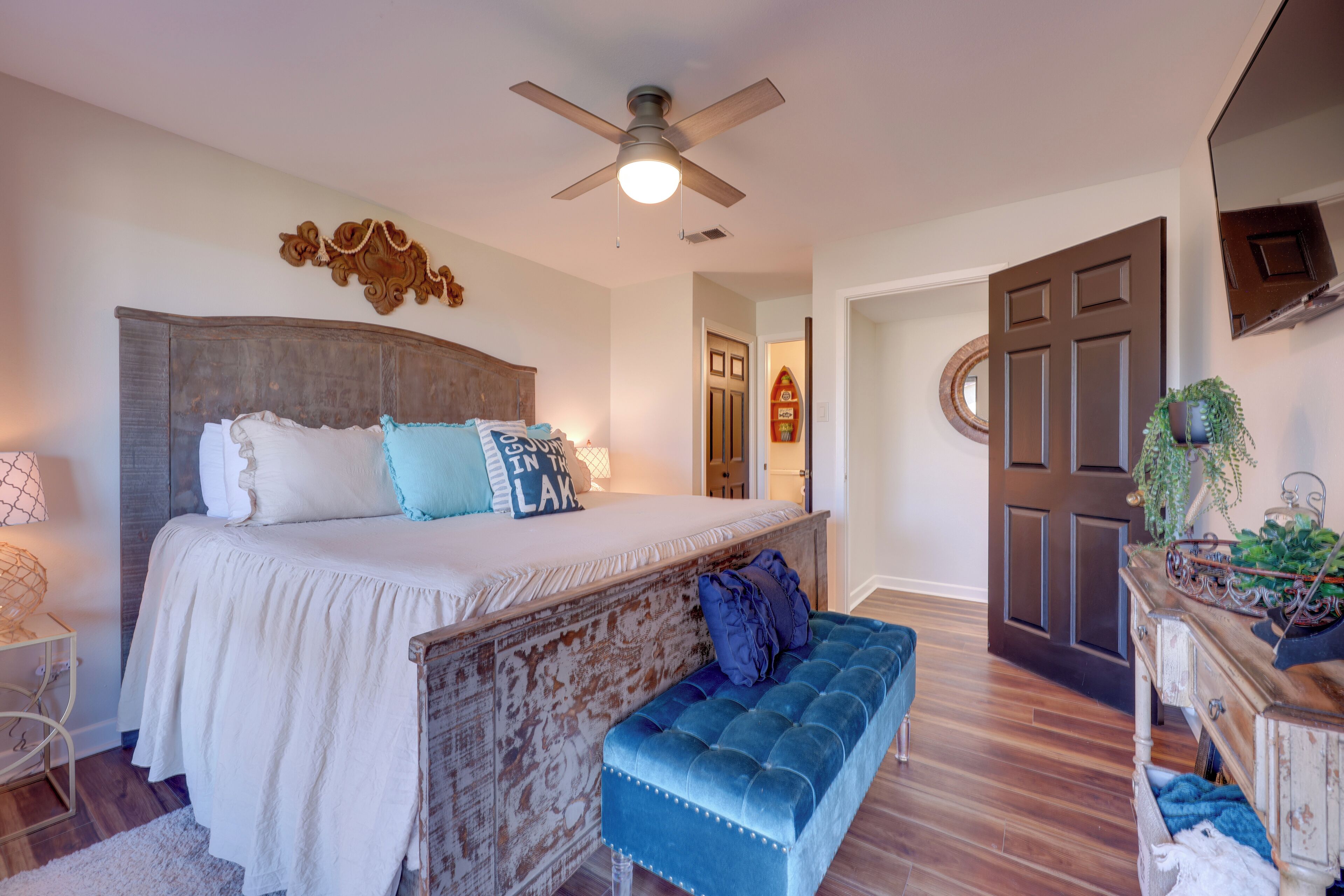 A bedroom with a large bed, a ceiling fan, a wooden headboard, and a blue bench.