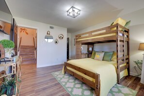 A bunk bed with a wooden frame and a yellow bedspread, a desk with a lamp, and a staircase leading to another room.