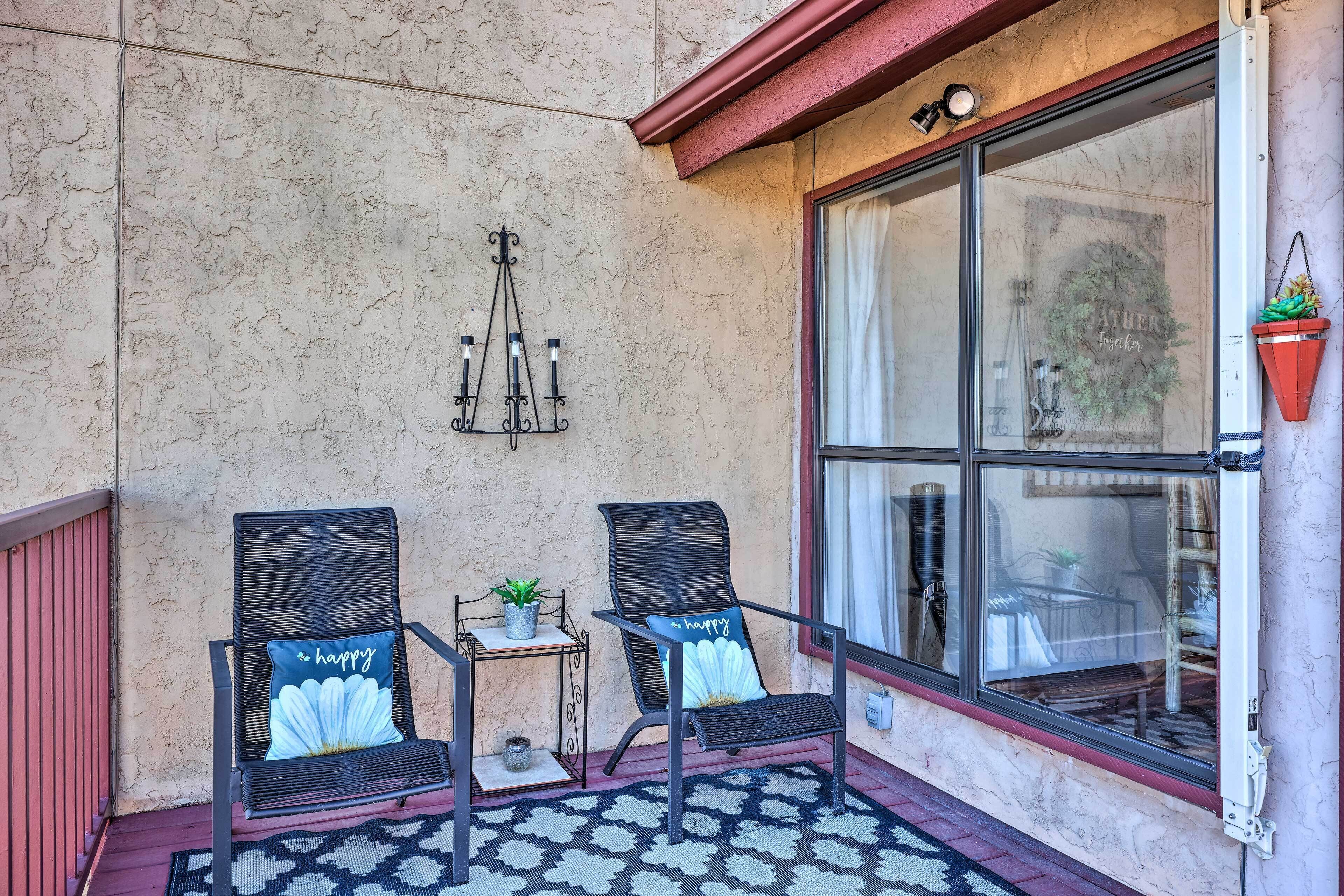 A patio with two chairs, a small table with a plant, and a decorative wall hanging.
