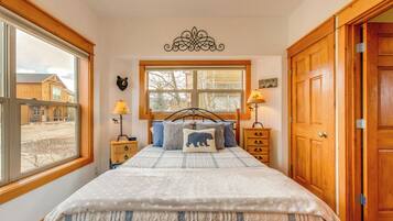 A bedroom with a large bed, wooden headboard, two bedside tables with lamps, a window with a view of buildings, and a wooden door.