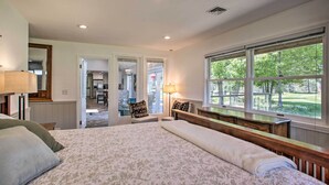 A bedroom with a large bed, a dresser, a nightstand, and a window with a view of trees. - All-seasons Chewelah Home: Fish, Golf & Ski! (Chewelah)