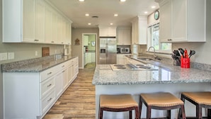 A modern kitchen with white cabinets, granite countertops, a stainless steel refrigerator, and a central island with stools. - All-seasons Chewelah Home: Fish, Golf & Ski! (Chewelah)