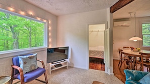 A cozy living room with a television, a dining table, and a large window with a view of trees. - Door County Retreat ~ 3 Mi to Sister Bay Beach (Sister Bay)