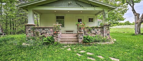 A green house with a porch, stone steps, and potted plants.