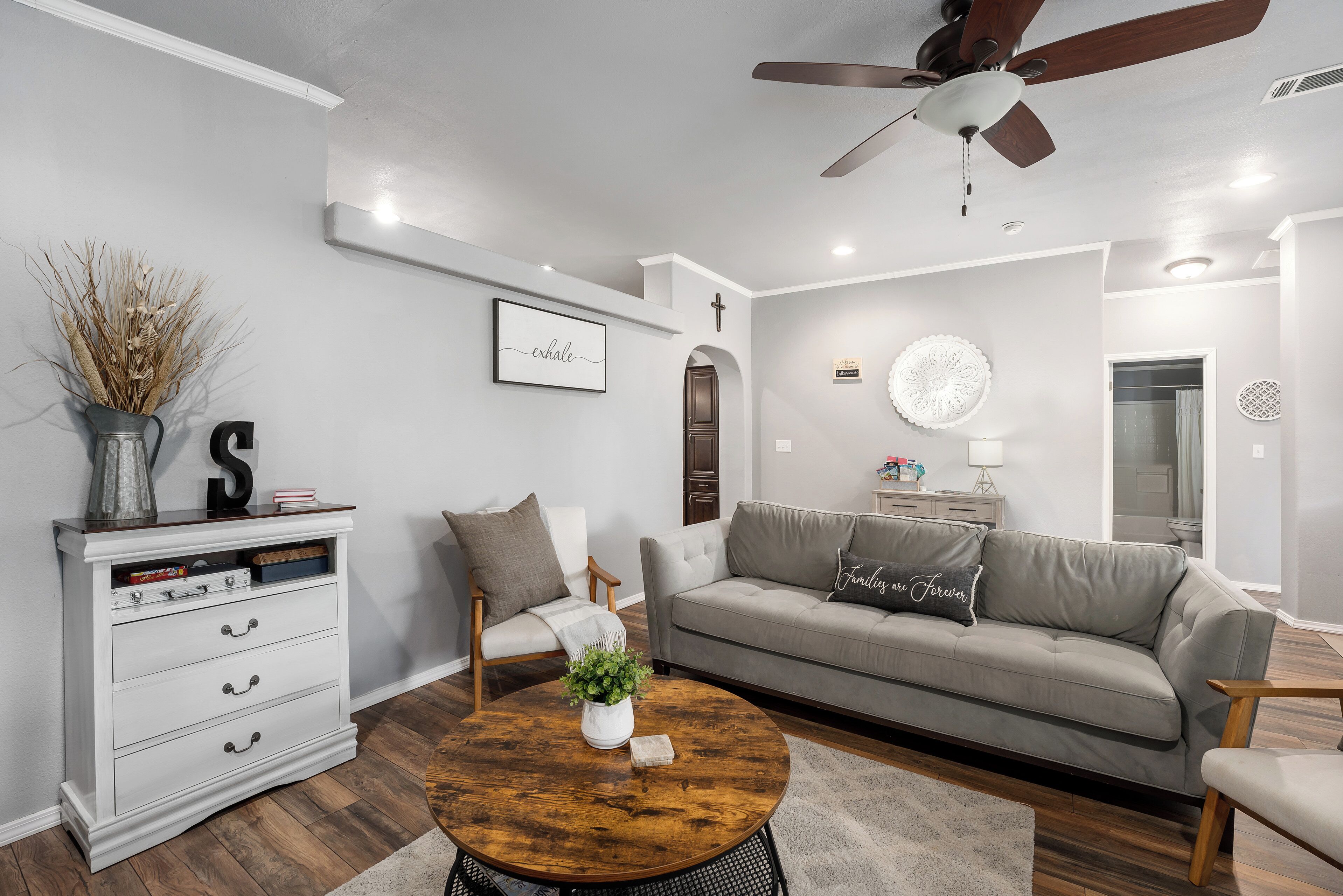 Una sala de estar moderna con un sofá gris, un aparador blanco y una mesa de centro redonda con una planta.
