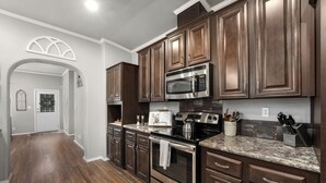 A modern kitchen with dark wooden cabinets, stainless steel appliances, and a granite countertop. - Hill Country Gem: Sunset Deck, Hot Tub & Fire Pit (Canyon Lake)