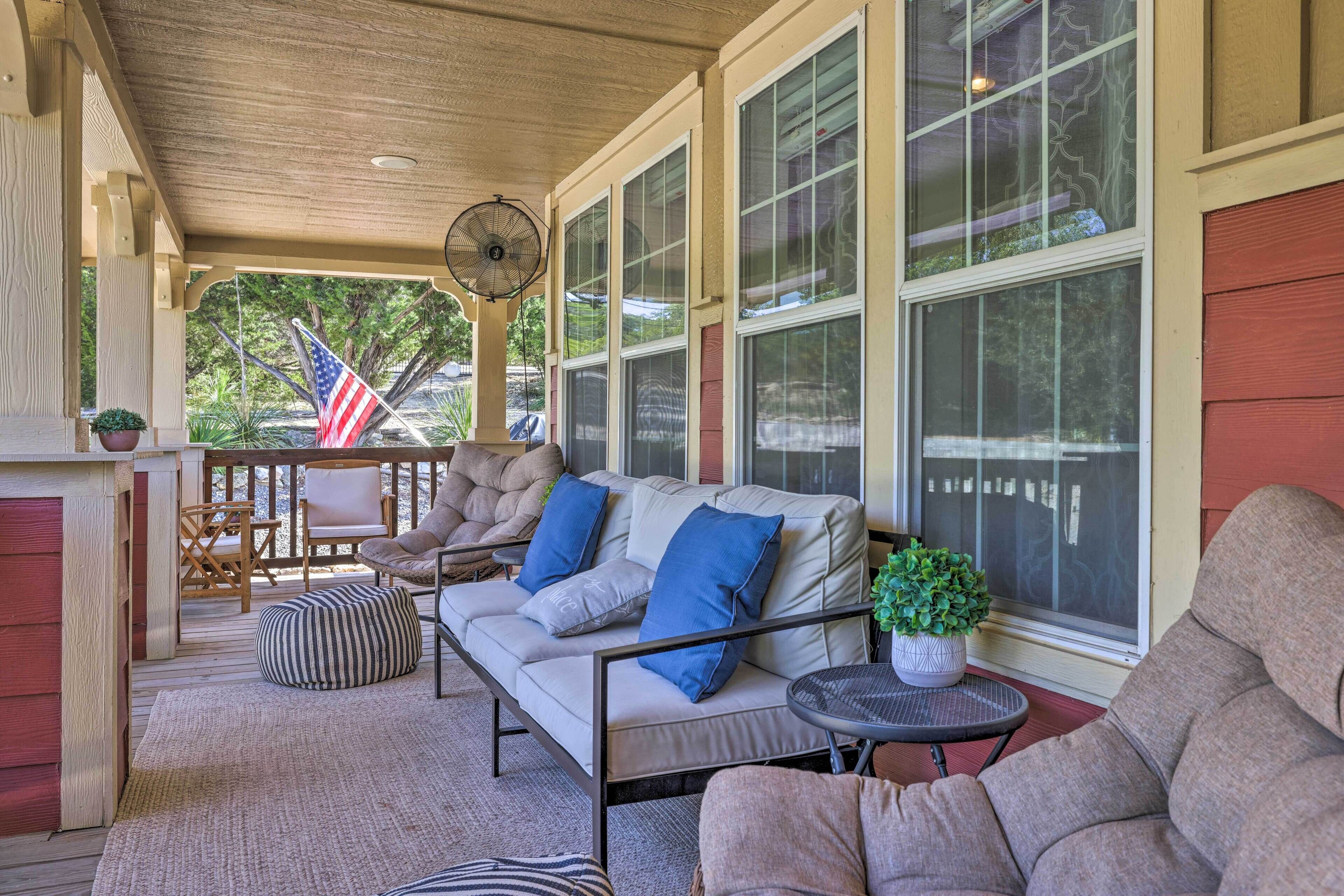 A covered porch with a sofa, chairs, a fan, and a small table with a plant.