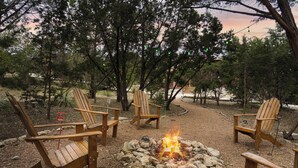 A fire pit surrounded by wooden chairs in a wooded area. - Hill Country Gem: Sunset Deck, Hot Tub & Fire Pit (Canyon Lake)
