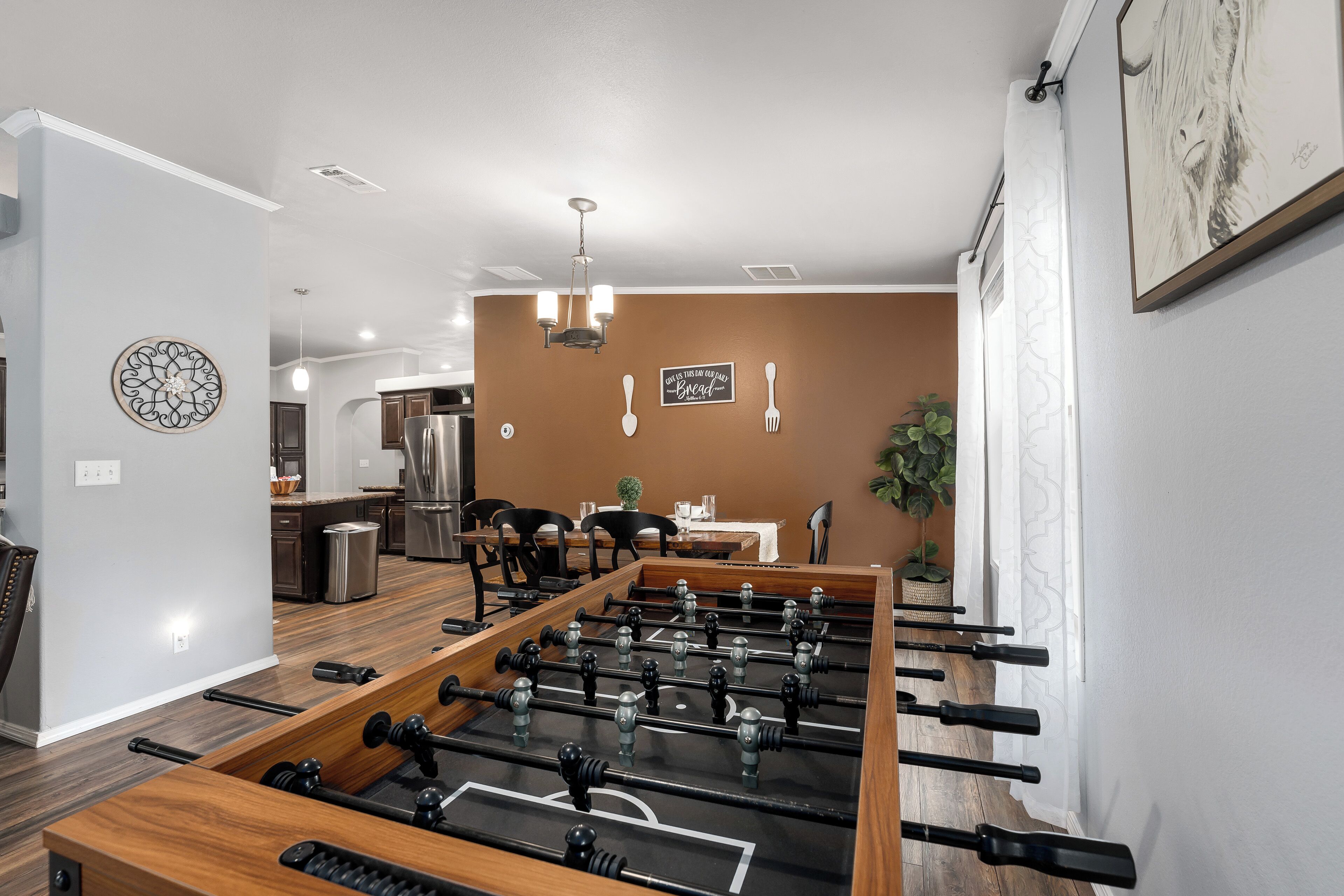 A modern kitchen with a foosball table, wooden cabinets, and a dining area with chairs and a table.