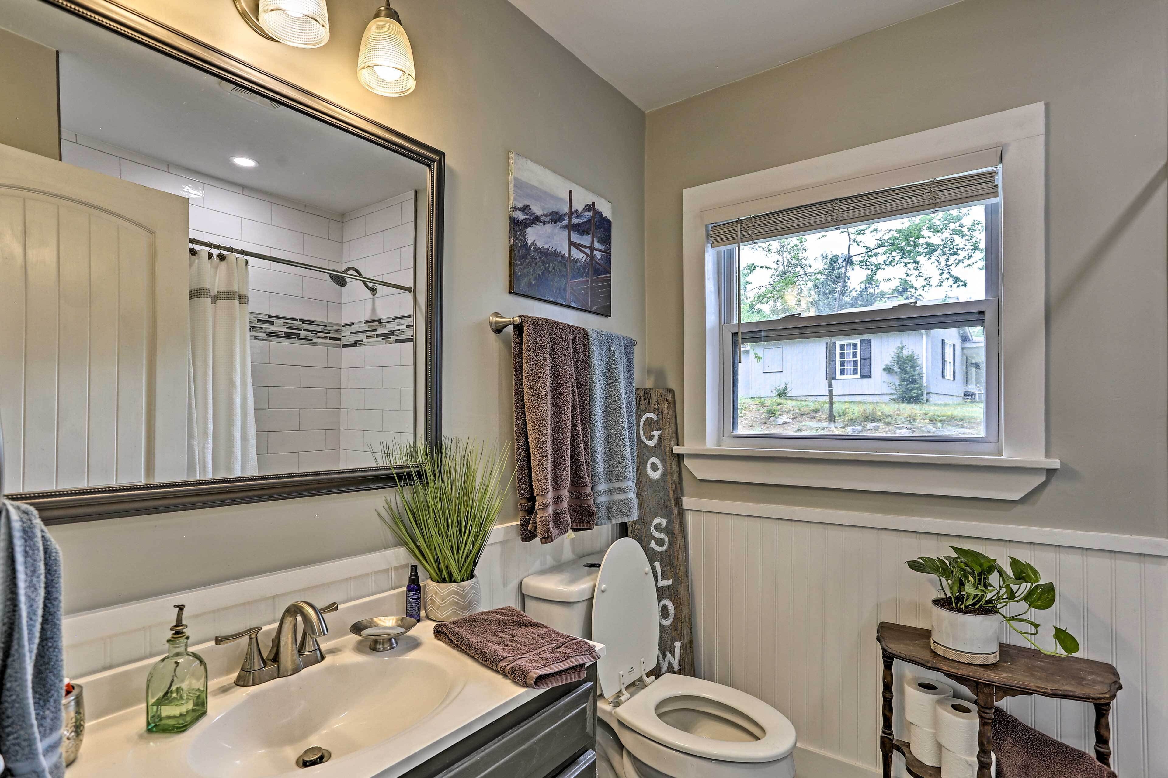 A bathroom with a white sink, a mirror, a toilet, a window, and a potted plant.