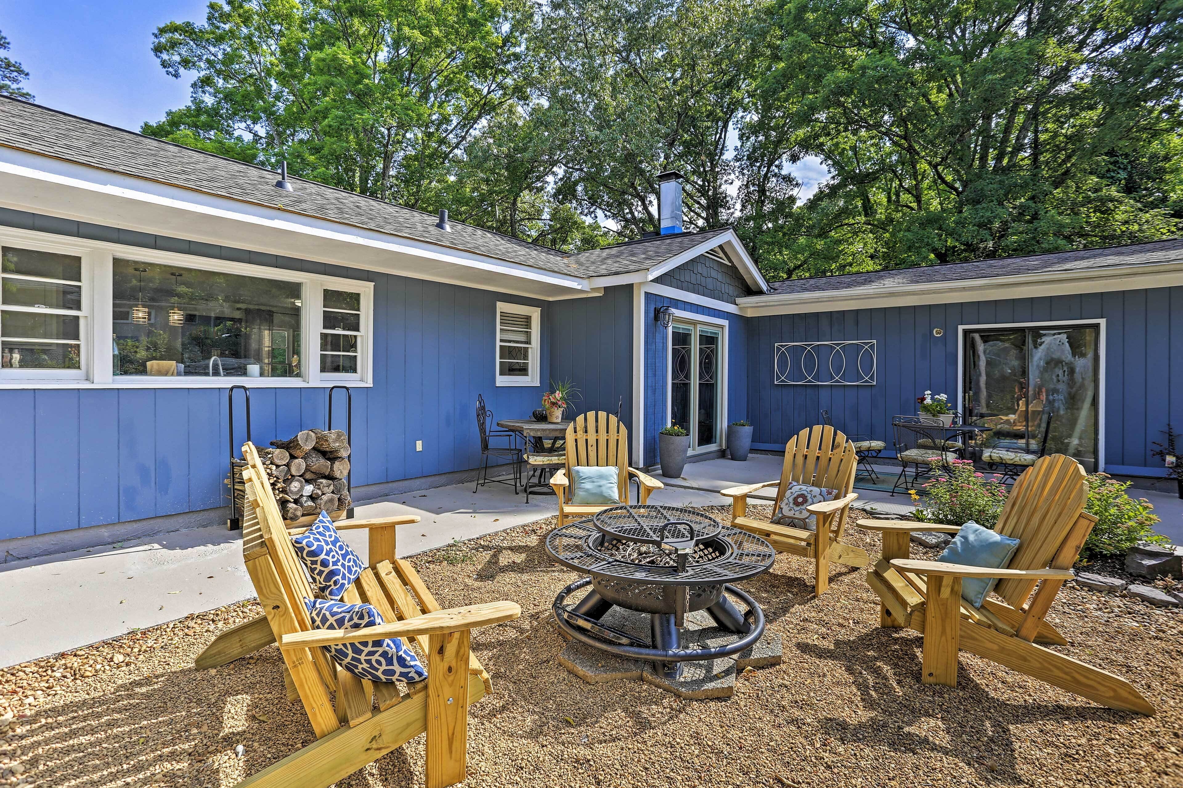 A blue house with a fire pit and wooden chairs in the backyard.
