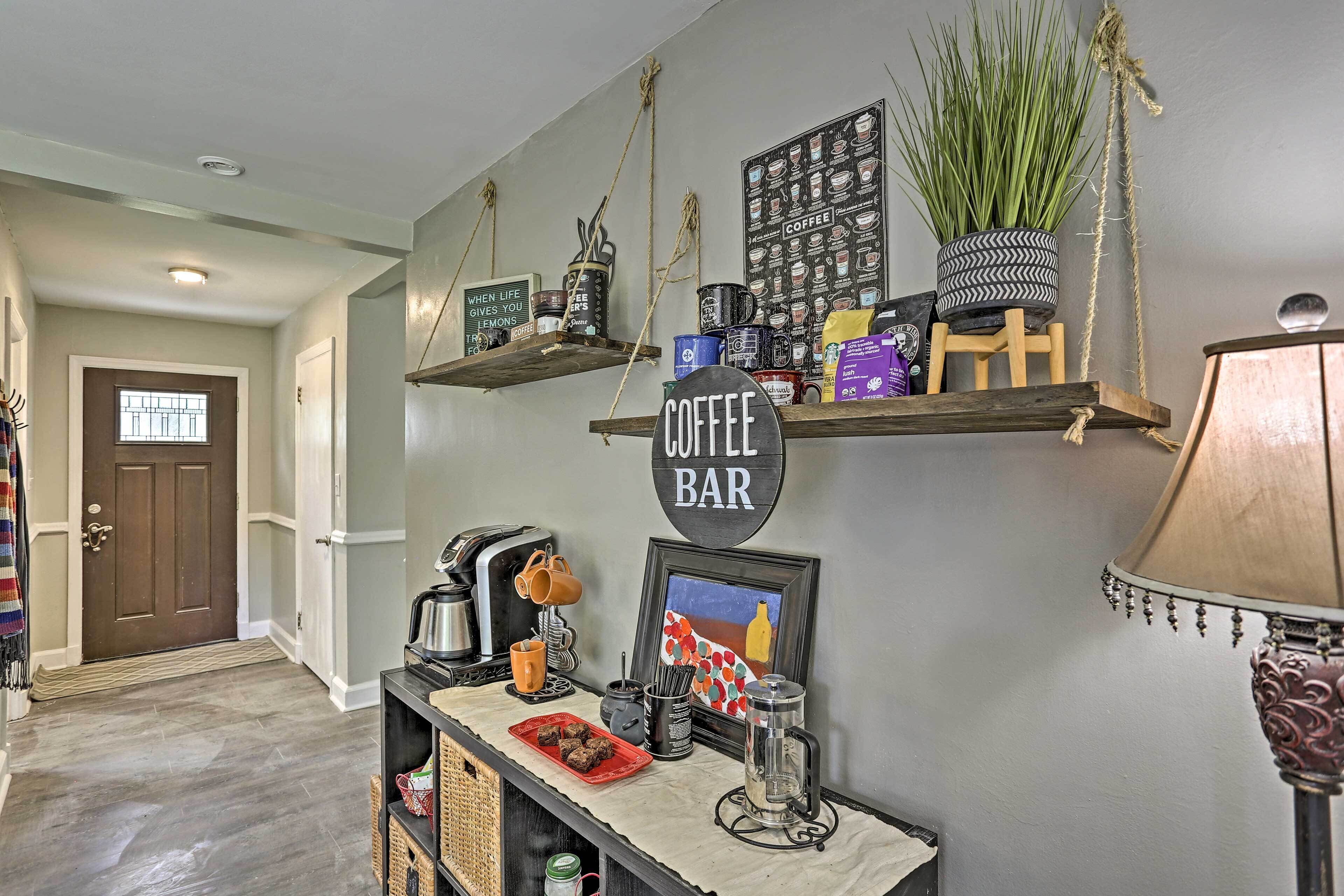 A hallway with a coffee bar area featuring a coffee-themed sign, shelves with coffee mugs, a coffee maker, and a framed picture.