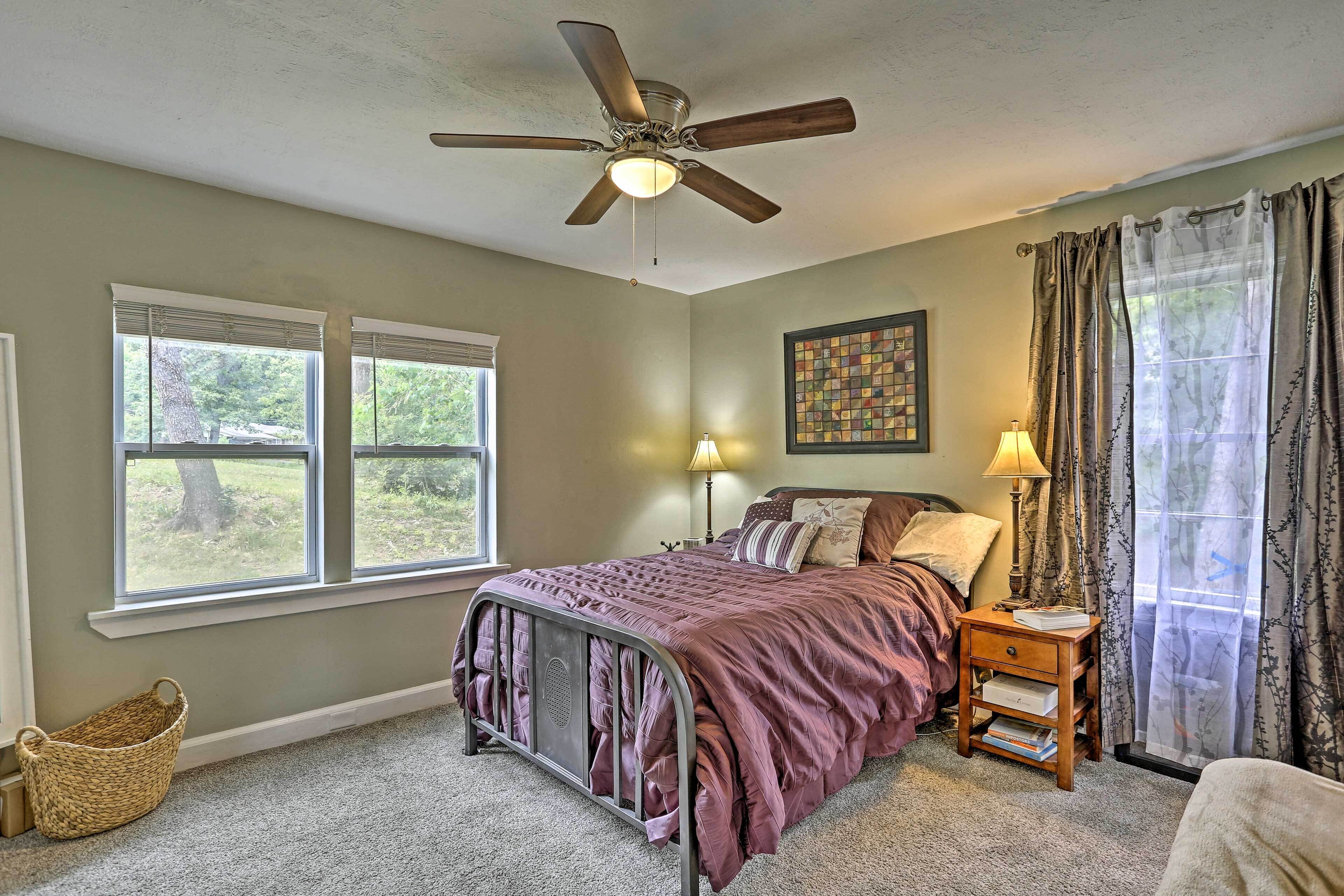 A bedroom with a bed, a ceiling fan, a nightstand with a lamp, and a window with blinds.