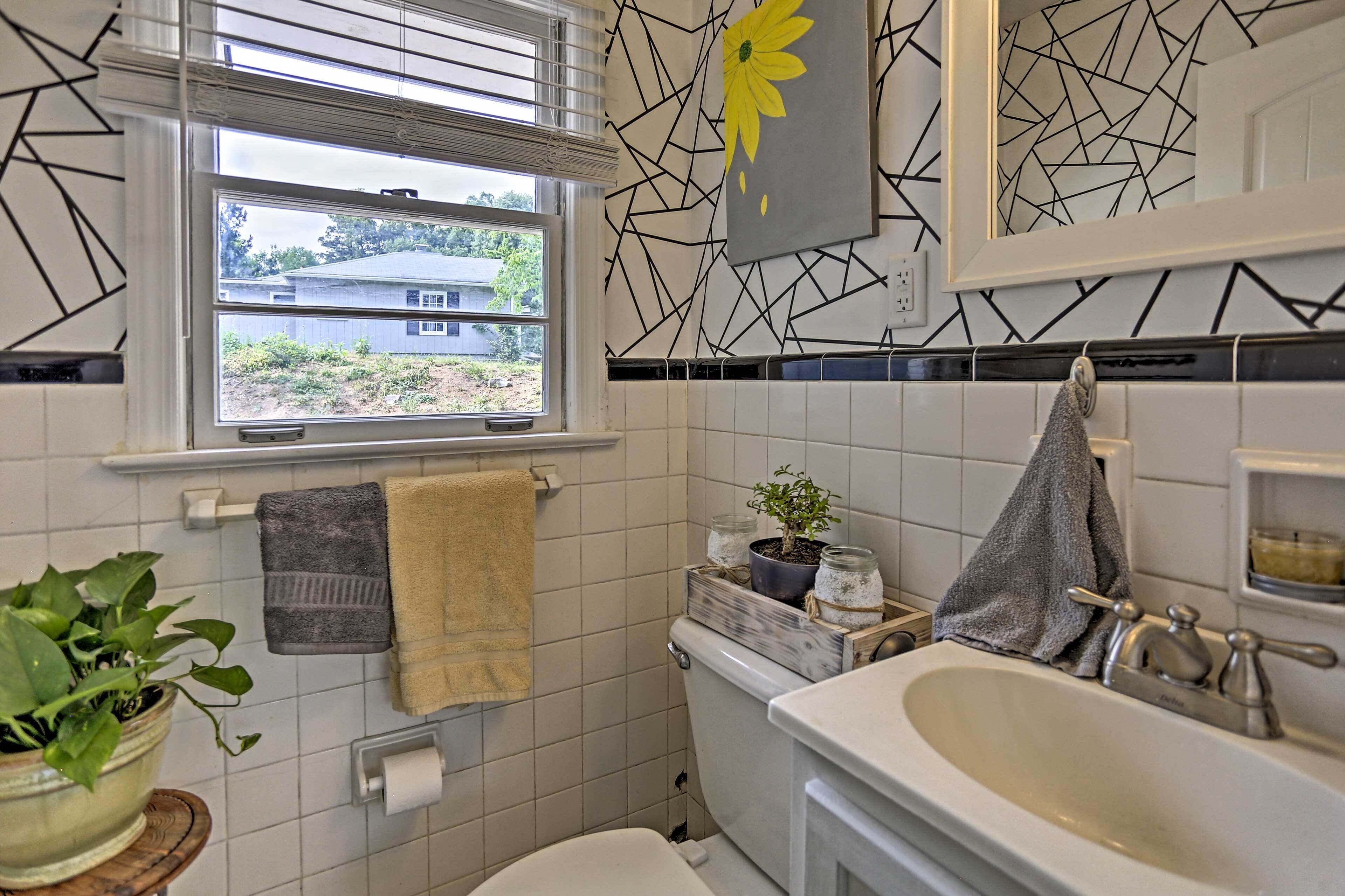 A bathroom with a window, a sink, and a toilet. There is a towel rack with towels and a potted plant.