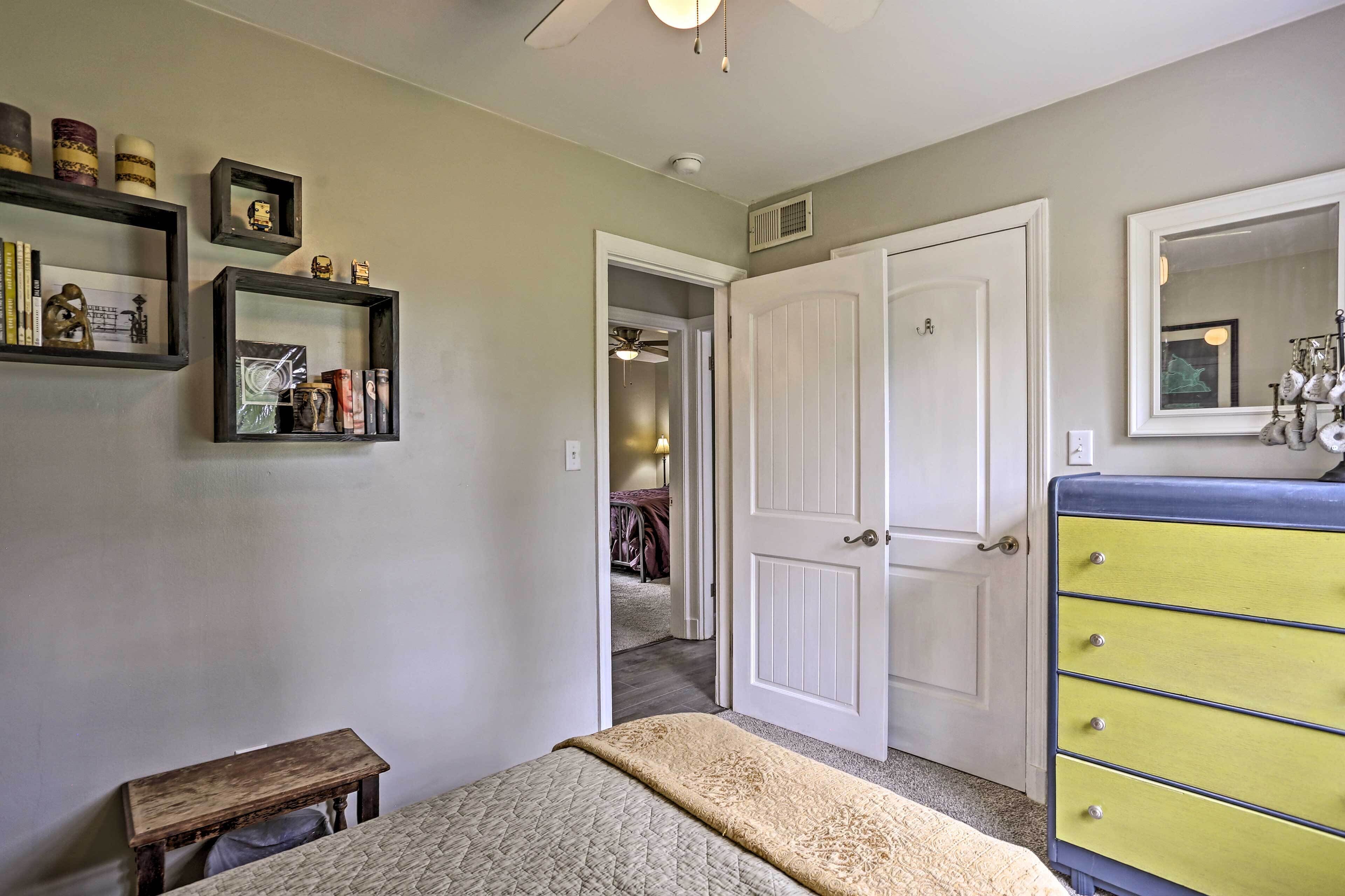 A bedroom with a bed, a wooden bench, a dresser, and shelves with decorative items.
