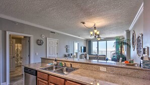 A kitchen with granite countertops, a dishwasher, wooden cabinets, a chandelier, and a large window overlooking a balcony.