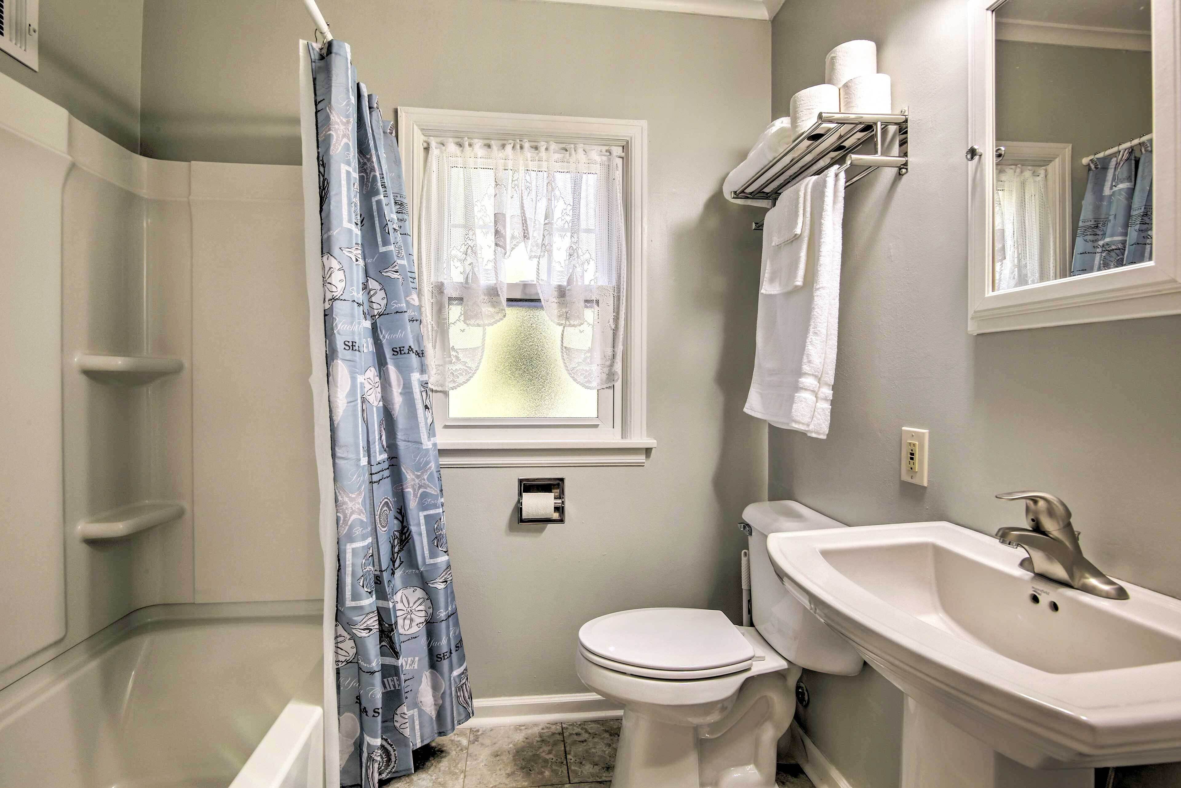 A bathroom with a shower, toilet, sink, and a window with a curtain.