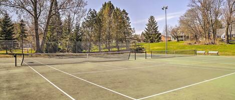 A tennis court with a net, surrounded by trees and a fence.