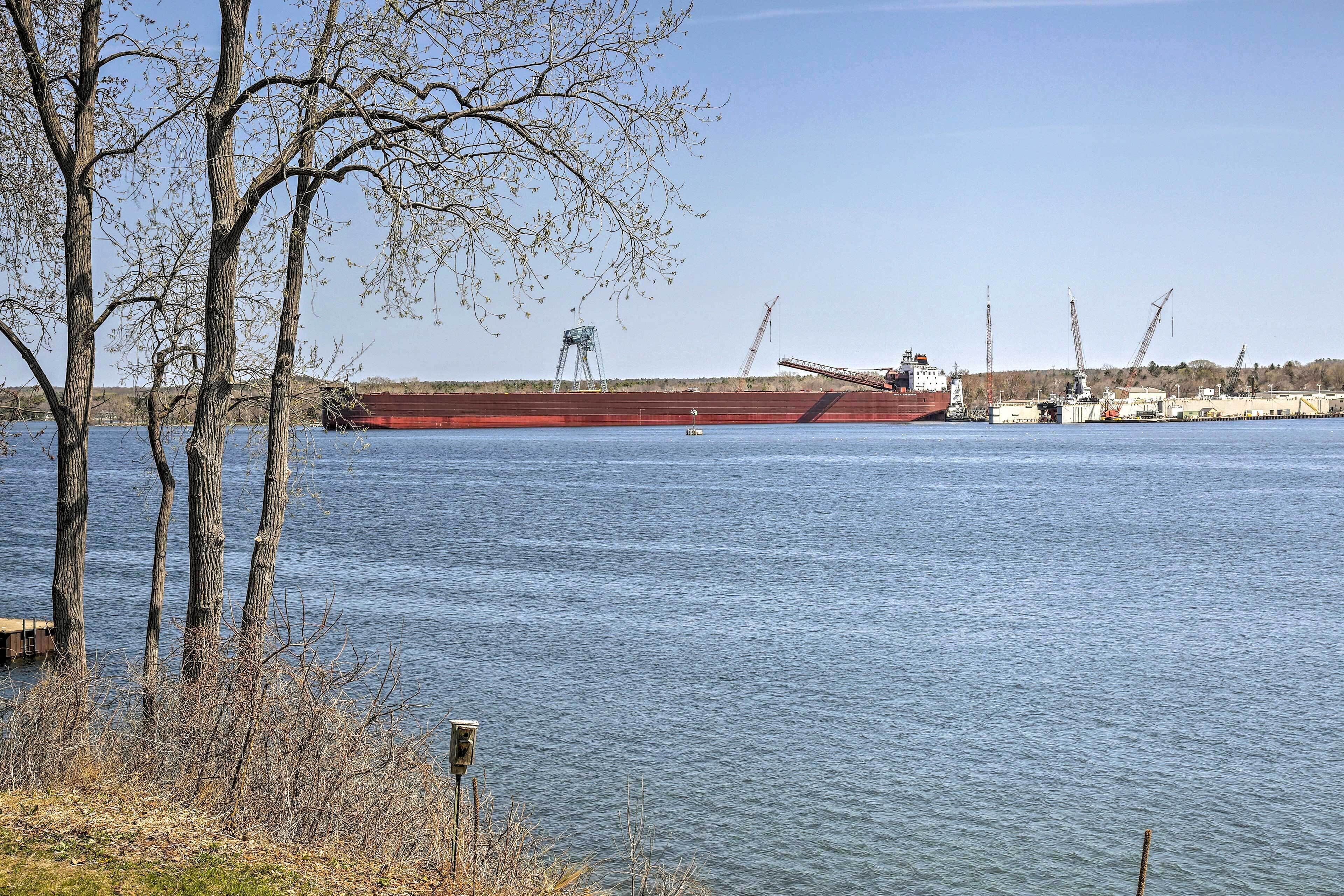 A large cargo ship docked at a port with cranes and industrial buildings in the background.