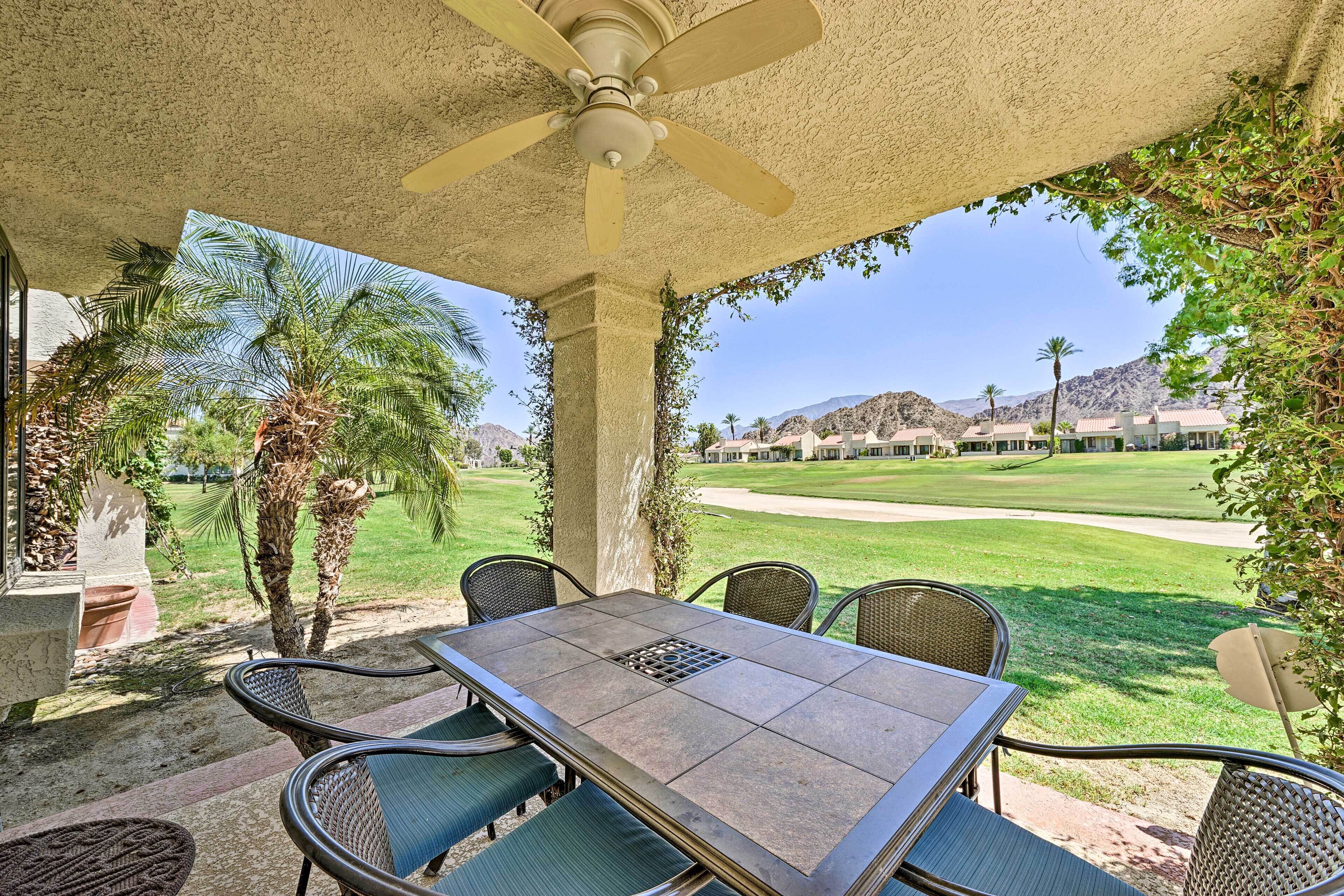 A covered patio with a table and chairs, overlooking a golf course.