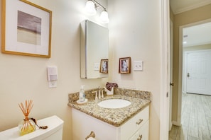 A bathroom with a white toilet, a sink with a granite countertop, a mirror, and a framed picture on the wall. - Pet-friendly Galveston Cottage < 1 Mi to Beach! (Galveston)