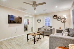 A living room with a flat-screen TV, a ceiling fan, a coffee table, and a gray sofa. - Pet-friendly Galveston Cottage < 1 Mi to Beach! (Galveston)