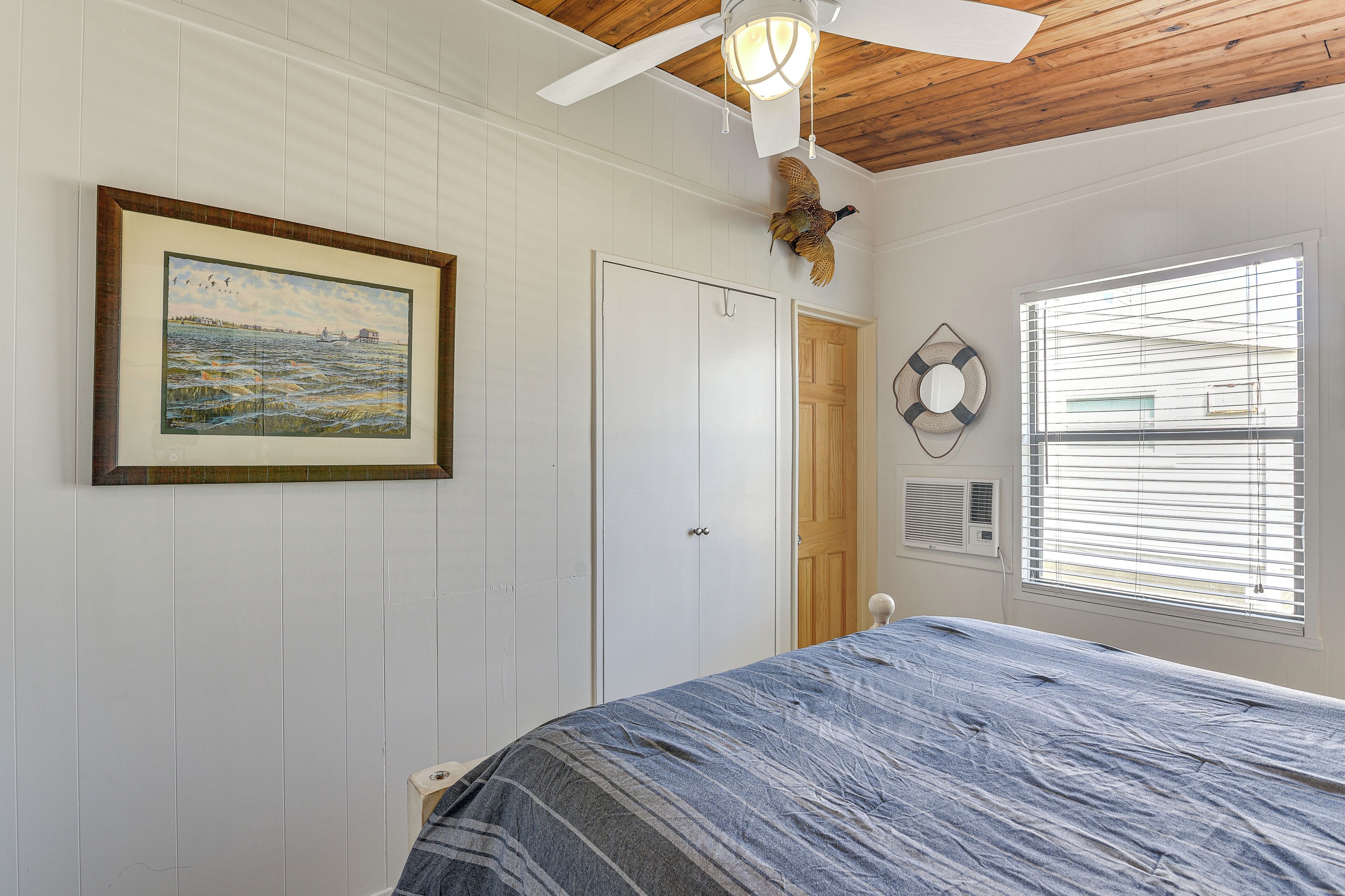 A bedroom with a bed, a ceiling fan, a window with blinds, a door, and a framed painting on the wall.