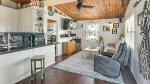 A spacious kitchen with white cabinets, a wooden ceiling, and a dining area with a gray sofa and patterned rug. - Walk to Sea Isle Beach: Updated Group Getaway! (Galveston)