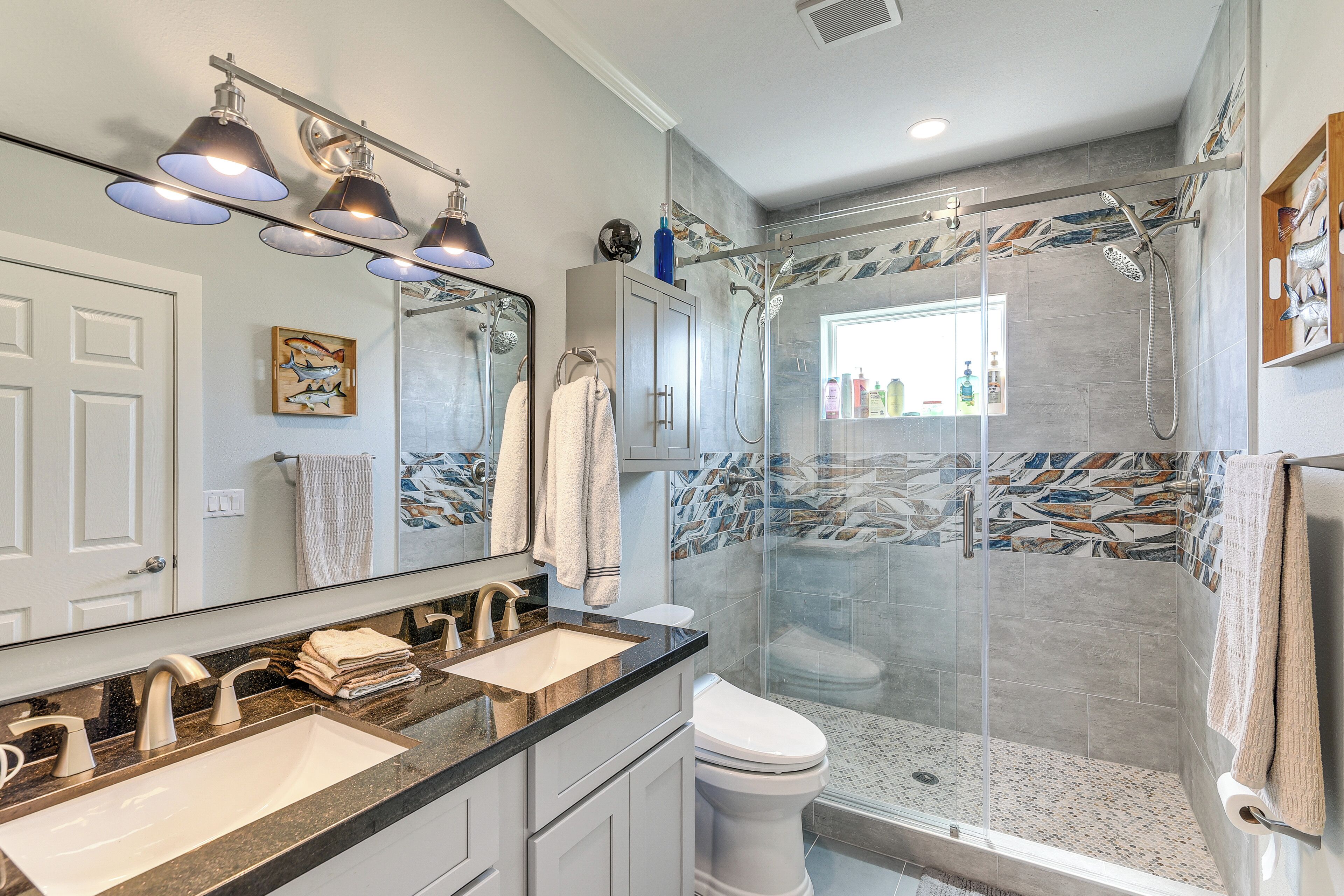 A modern bathroom with a double sink, a toilet, and a glass-enclosed shower area.