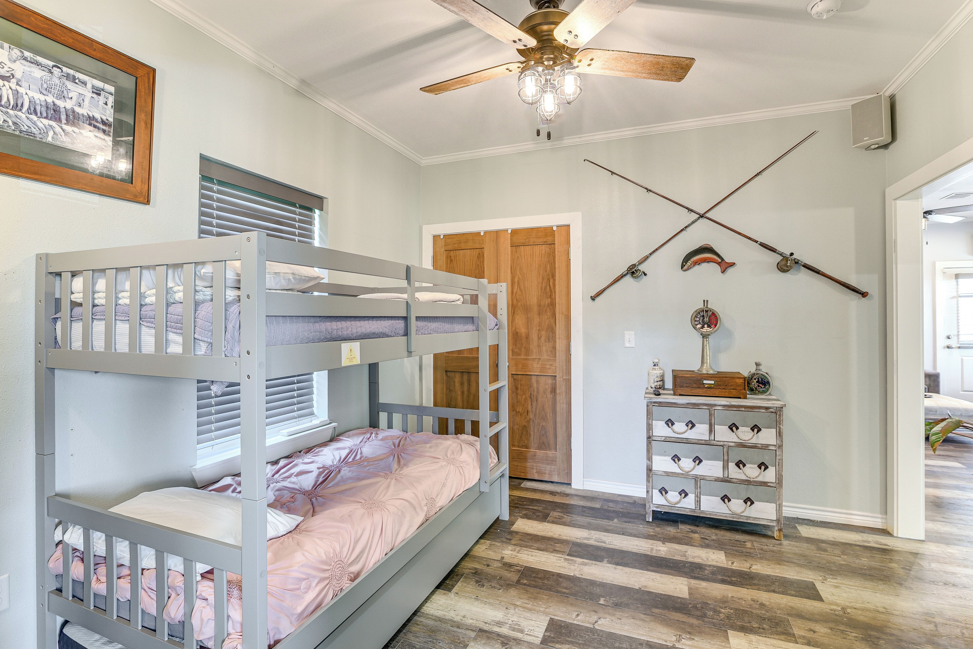 Habitación con literas, ventilador de techo, puerta de madera y cómoda con ganchos.