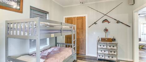 Habitación con literas, ventilador de techo, puerta de madera y cómoda con ganchos.
