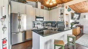 A modern kitchen with white cabinetry, stainless steel appliances, and a central island with stools. - Walk to Sea Isle Beach: Updated Group Getaway! (Galveston)