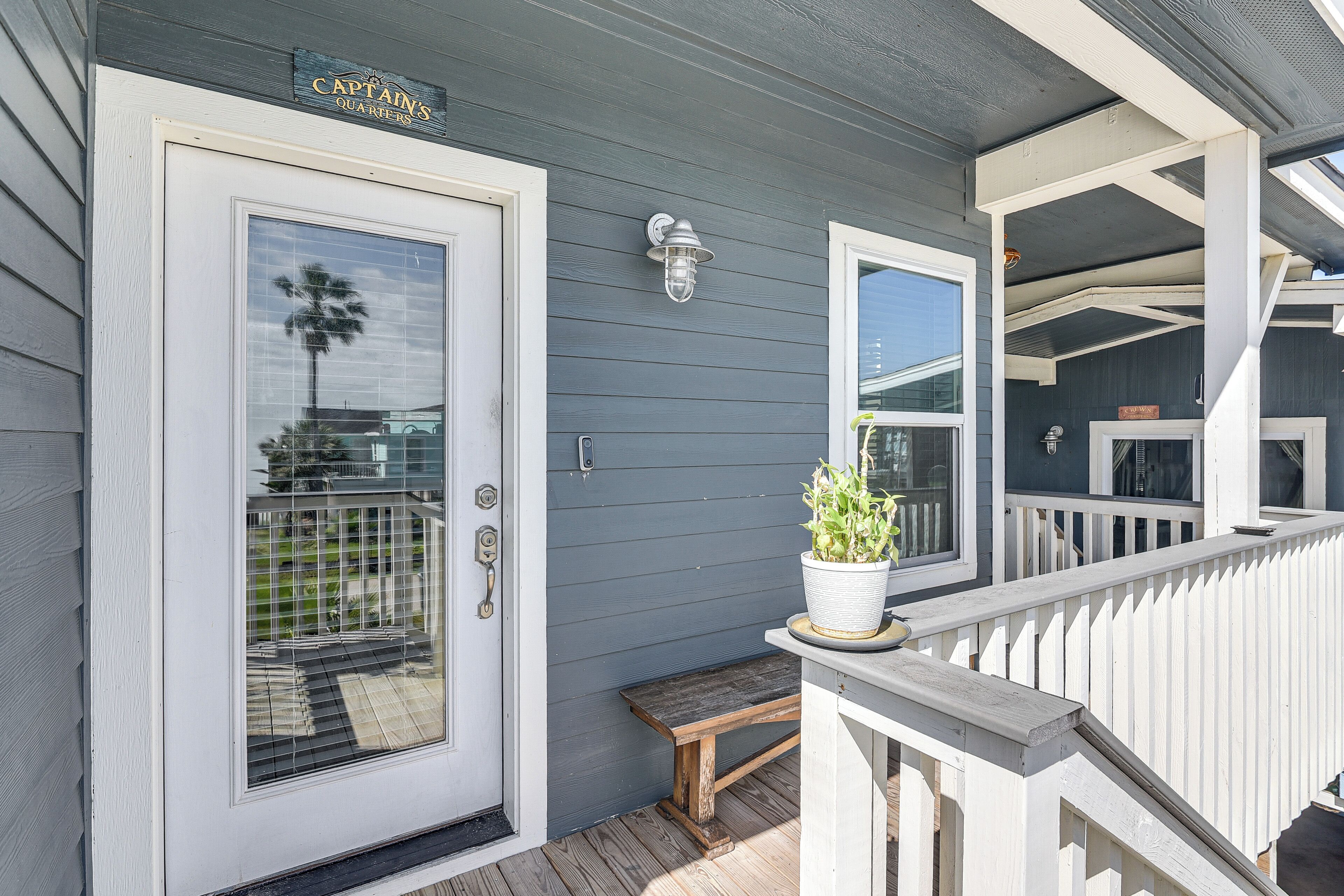 A house with a gray exterior, a white door, a bench, and a potted plant on the porch.