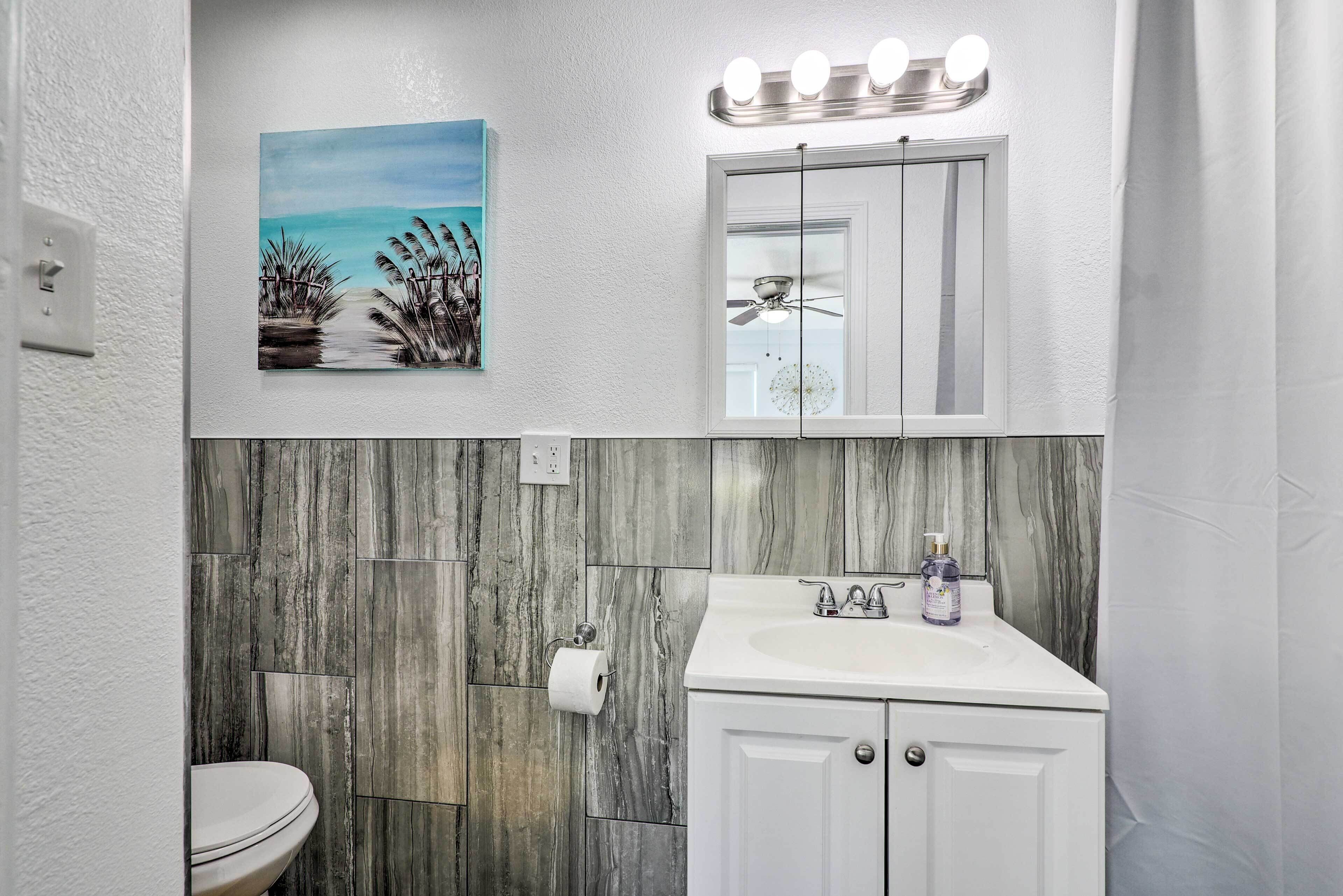 Un baño con inodoro blanco, lavabo con espejo arriba y un cuadro de una playa.