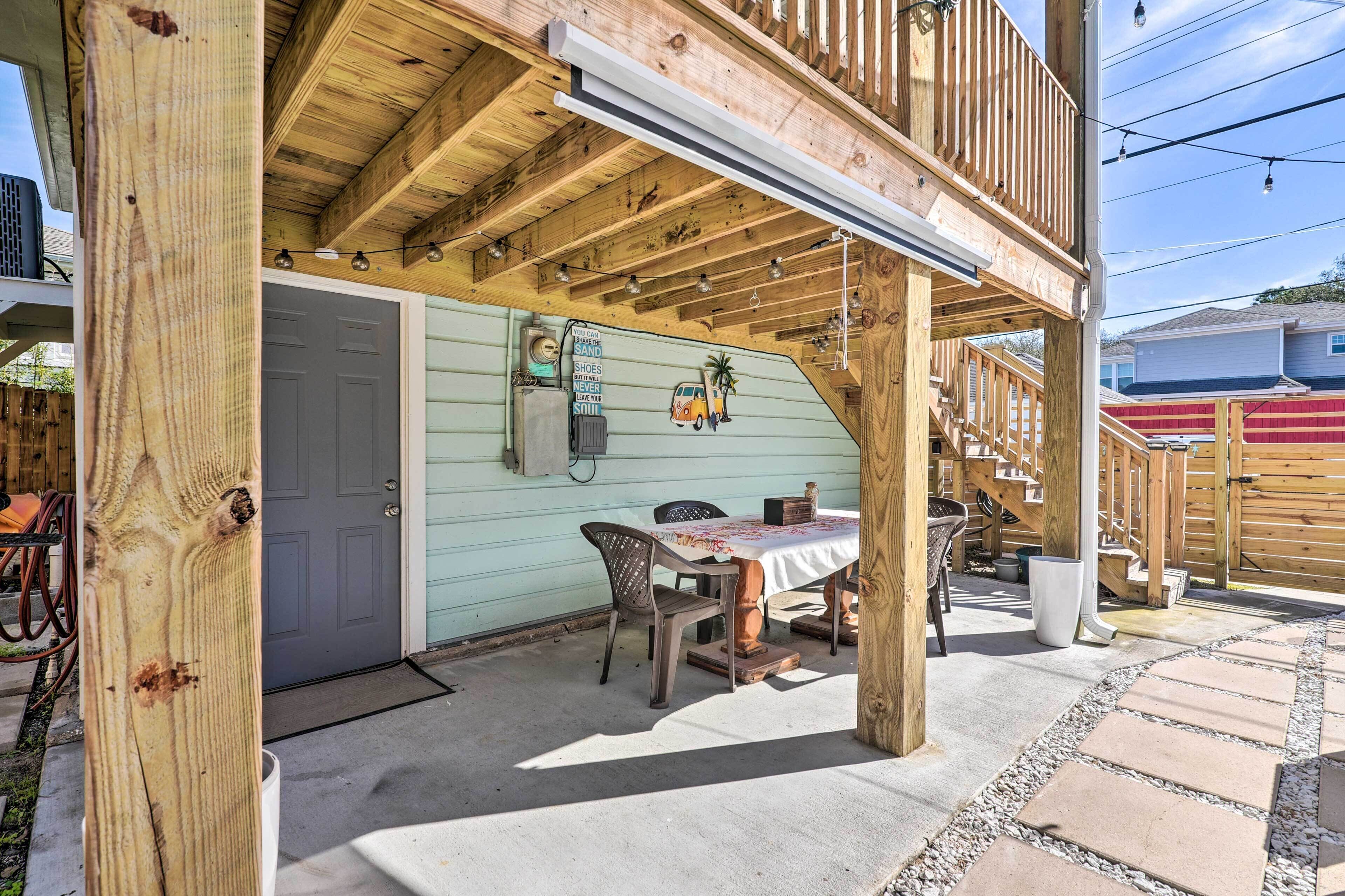 A wooden deck with a table and chairs, a door, and a staircase leading to a second level.