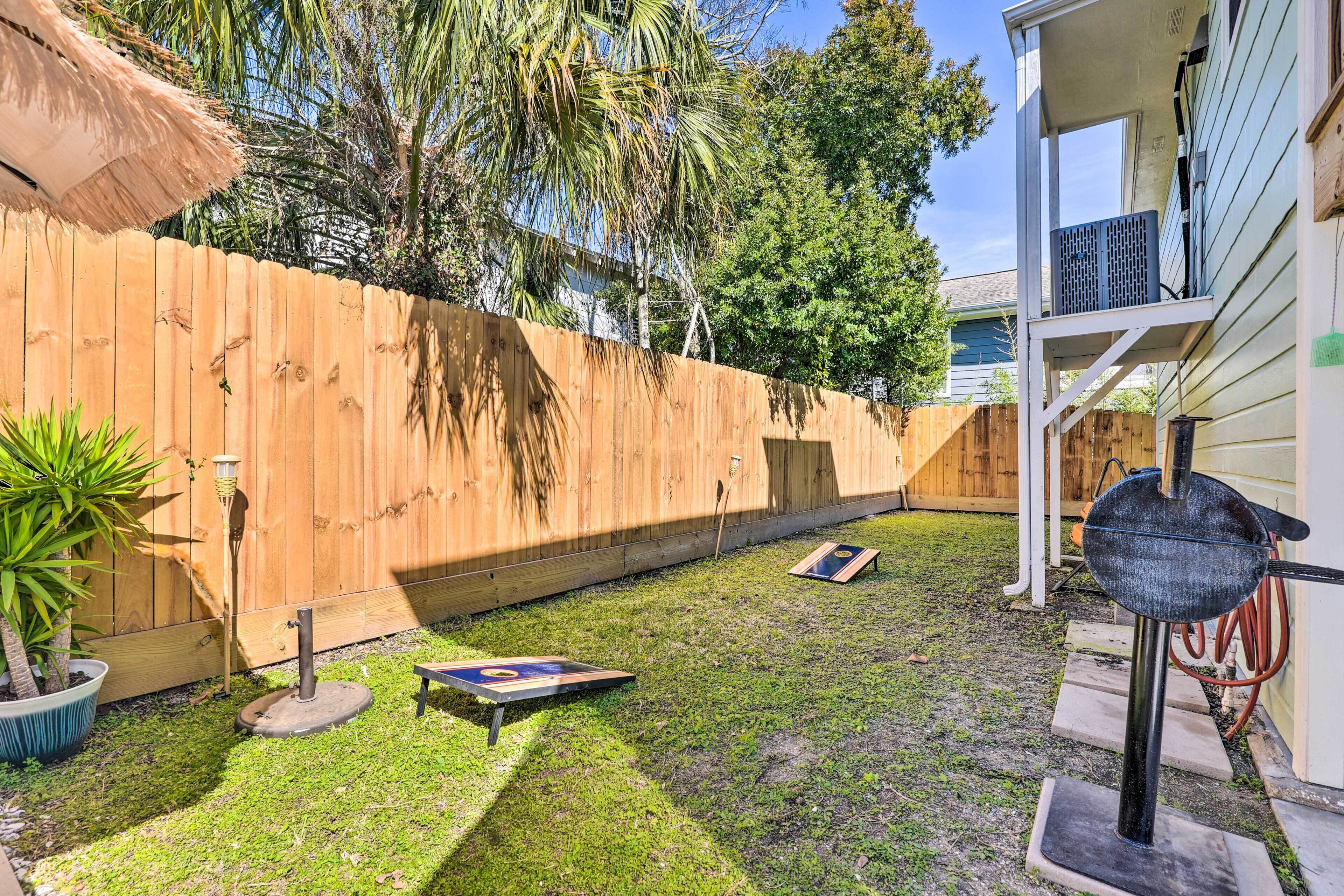 A backyard with a wooden fence, a thatched roof, a grill, and a hose.
