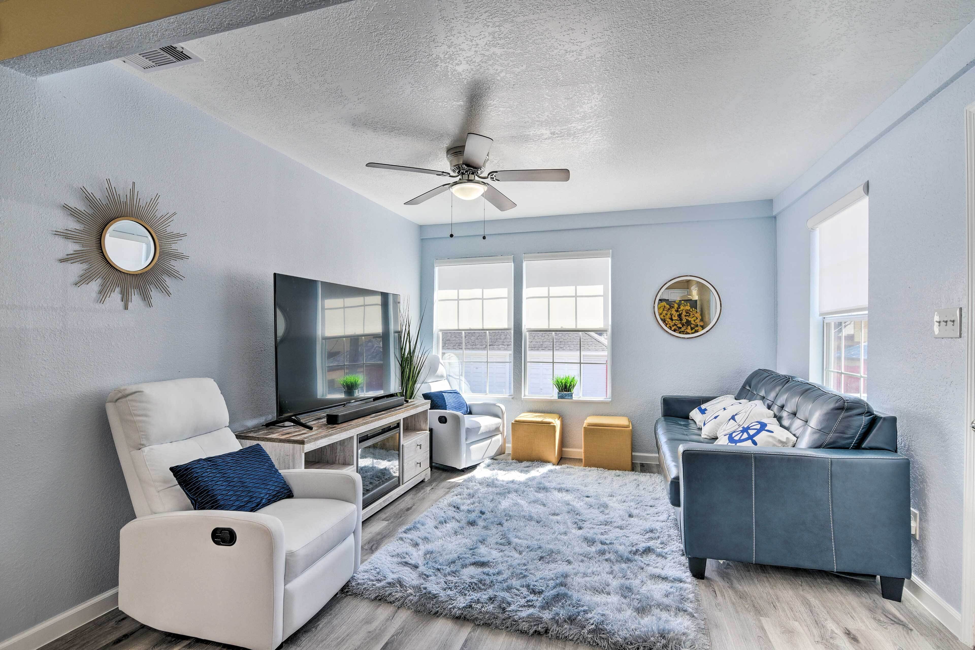 A living room with a white recliner, a blue sofa, a ceiling fan, a TV, and a large window.