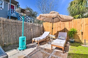 A backyard with two lounge chairs, a tiki-style umbrella, and a blue heater.