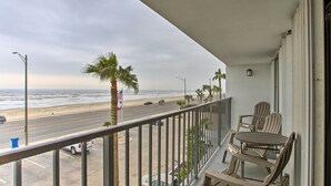 Een balkon met uitzicht op het strand, een tafel met stoelen en een vlag.