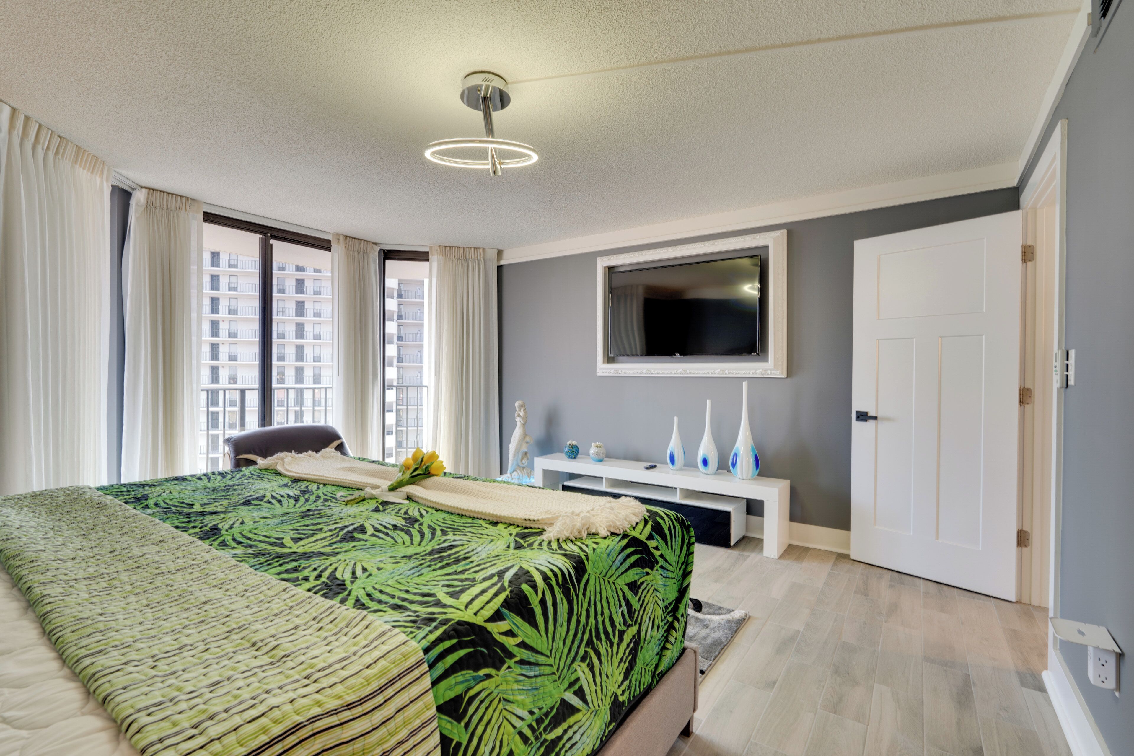 Un dormitorio moderno con una cama grande, un televisor montado en la pared y una puerta blanca.